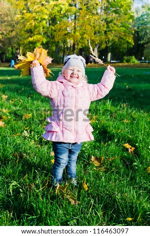 The little girl collects fallen down leaves in autumn park