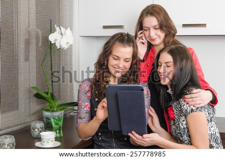 Three young women friends chatting at home and using laptop to look at new photo or browsing internet for information