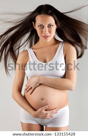 Young pregnant woman with flying hairs in white maternity wear