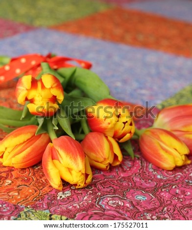 A simple bouquet of spring yellow and red  tulips, tied with red spotty ribbon, laying on an Indian cotton patchwork bedspread, a flower arrangement for mother\'s day , Easter or valentines