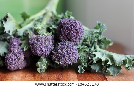 Organic purple sprouting broccoli on a wooden kitchen chopping board in a domestic kitchen, preparing fresh vegetables