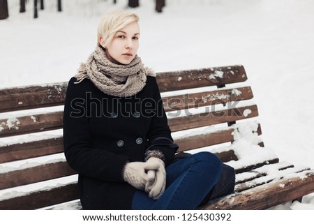Young beautiful girl is sitting alone on the bench in winter park