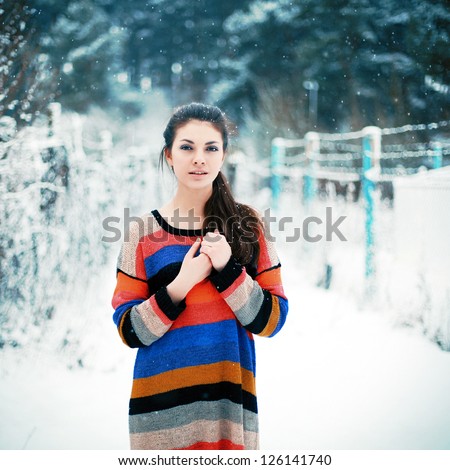 Young pretty girl standing in winter on the street. Snow falls on her hear