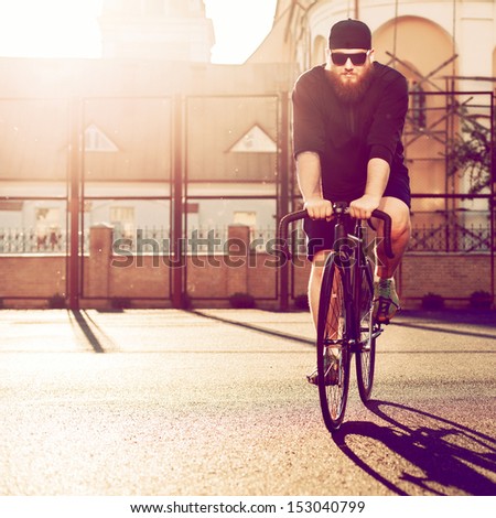 Young fashion outdoor portrait of young bearded hipster posing in summer on the street driving cool custom fixed gear bike in evening sunlight