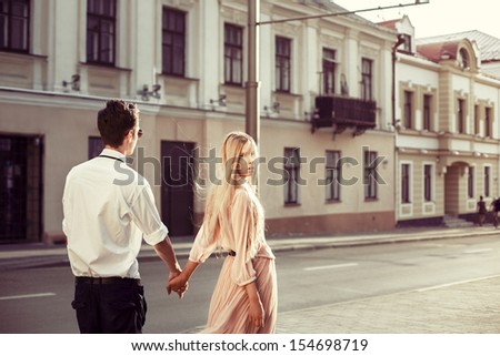 Young fashion elegant stylish couple posing on streets of european city in summer evening weather. Sensual blonde vogue girl with handsome hipster man walk on the road in europe