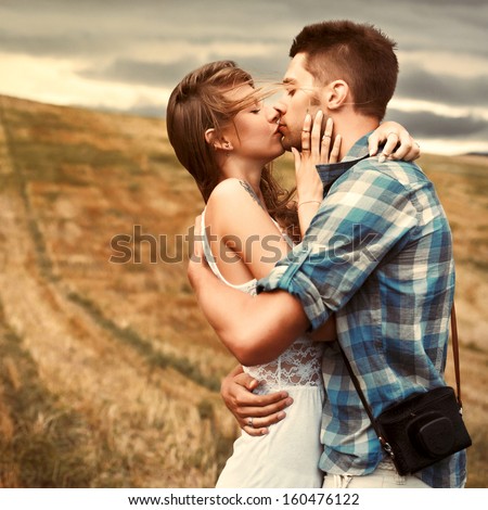 Stunning sensual outdoor portrait of young stylish fashion couple kissing in summer in corn field behind rainy clouds and storm.