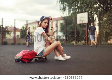 Sport fashion girl posing in summer with skateboard and backpack in university. Hipster bright color portrait