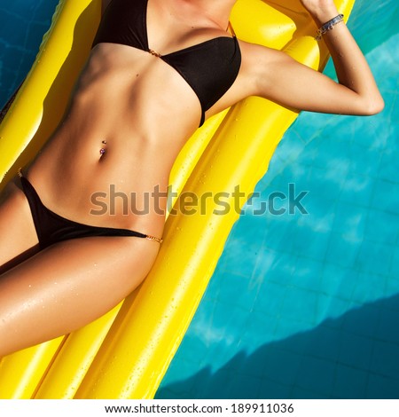 Young pretty fashion woman body posing in summer in pool with clear water lying on mattress in black bikini and having fun