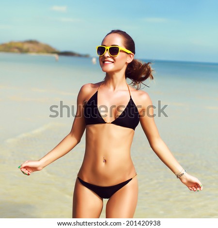 Pretty young woman running alone with happy smile in black bikini on the beach near the sea and blue sky and have fun