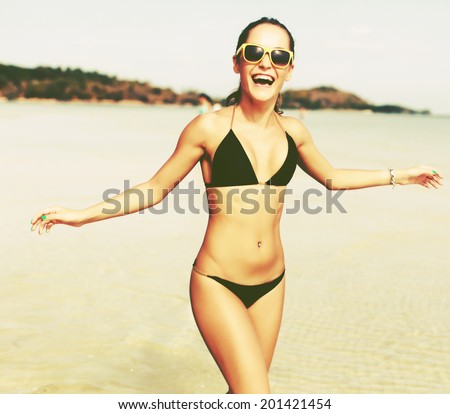 Pretty young woman running alone with happy smile in black bikini on the beach near the sea and blue sky and have fun