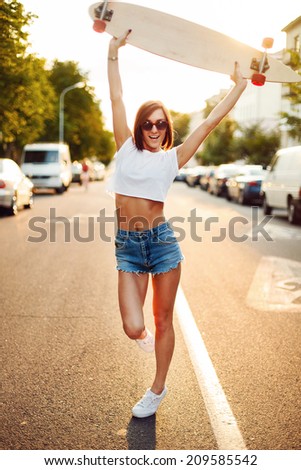 Young pretty sport woman in short jeans shorts posing and smiling on the street in summer with longboard and screaming of happiness