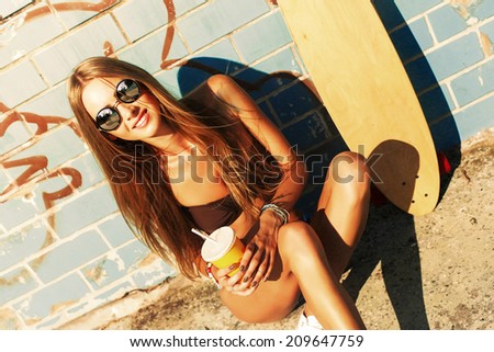 Pretty young blonde woman sitting and smiling with pretty face near the beach with longboard and cocktail in summer in hot sexy bikini and have fun alone travel style