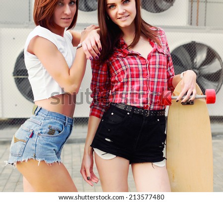 Outdoor colorful vintage portrait of two pretty fashion girls friends dressed in sexy shorts sensual photo with longboard urban style