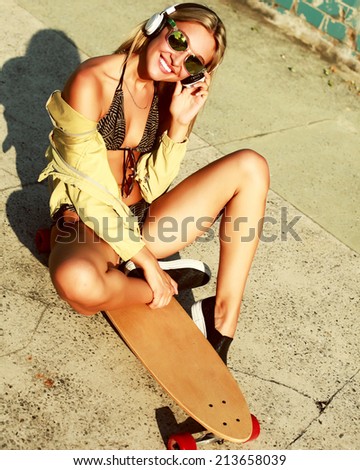 Beautiful sexy hot blonde girl smiling having fun listening music in summer outdoor in hot weather sitting on longboard lifestyle pics