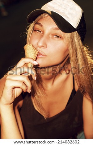 Young sexy blonde girl eating chocolate ice cream in summer hot weather in baseball hat  have fun and good mood looking in camera and smiling with sexy eyes look