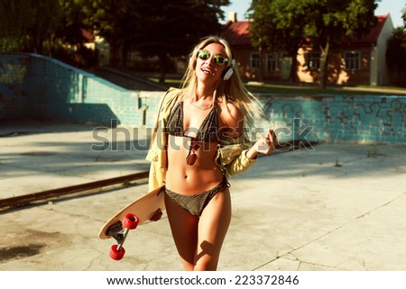 Pretty young smiling woman walking on the beach in hot  summer in bikini with longboard desk and have fun