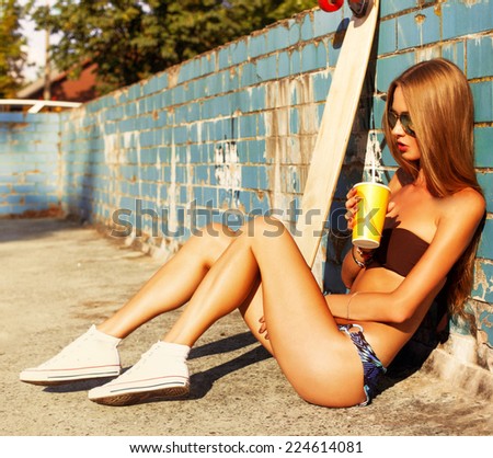Outdoor fashion summer portrait of pretty young blonde woman sitting in old pool and drinking cool cocktail and dreaming and have fun