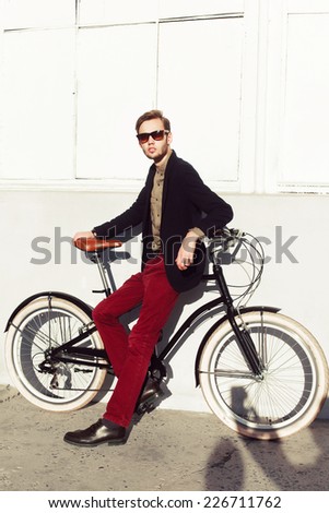 Outdoor summer fashion portrait of young stylish handsome man vintage retro style posing on the street white background with bicycle cruiser and have fun alone