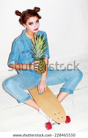 Young pretty sensual crazy girl posing on white background with green pineapple sitting on longboard dressed in jeans outfit colorful makeup and have fun