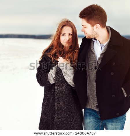 Young couple in love walking in cold winter field and getting cold but feels happy together