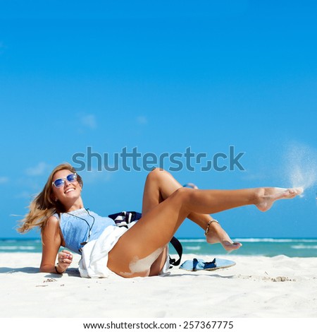 Outdoor summer portrait of young pretty sexy tanned woman lying and smiling having fun on the beach on white sand