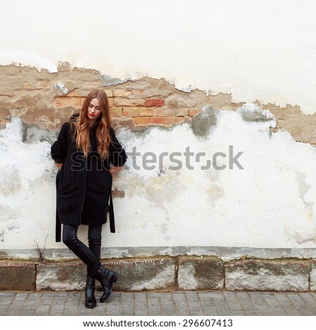 Young fashion sensual woman posing on the street near old brick wall background in black coat feels sad and alone depressed photo