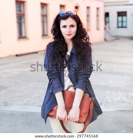 Pretty young brunette woman posing outdoor in autumn dressed in light coat with leather handbag looks stylish have fun in Europe in spring