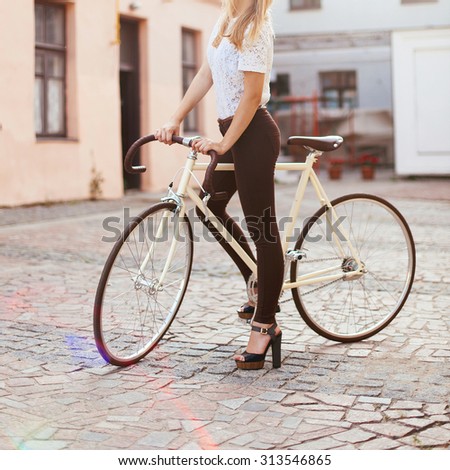 Outdoor fashion portrait of pretty young blonde woman posing outdoor on the street and have fun with white vintage style bicycle