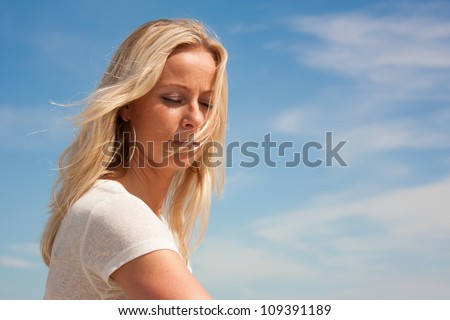 Young beautiful woman in deep thoughts against a blue peaceful sky