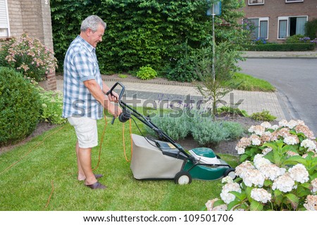 Dutch senior smiling and mowing his front yard grass with an electric mower as spare time activity after retirement