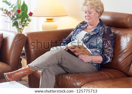 Senior Woman Sitting On Brown Leather Couch In Living Room Reading A ...