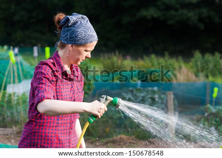 Young woman using a garden hose nozzle to water the allotment