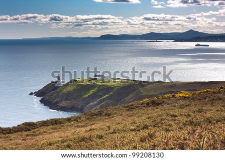 Green cliffs with a lighthouse and a ship anchored in a bay