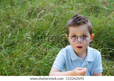 Little boy in a grass field with a blank expression