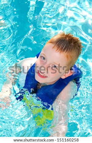 boy in swimming pool smiling, wearing a life vest