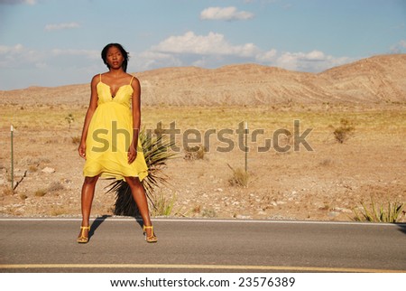 Full length shot of a beautiful African American woman wearing a yellow summer dress in the desert.