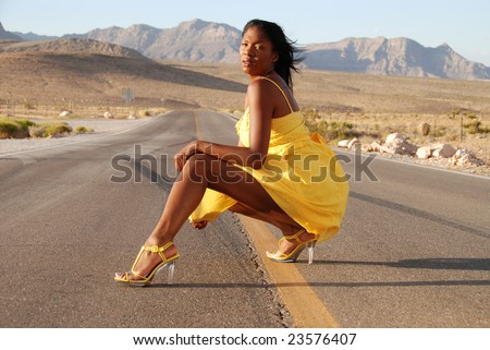 Sexy African American woman wearing a yellow summer dress posing in the middle of the road in the desert.