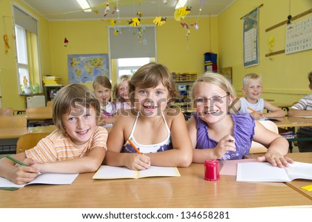 Children in a yellow classroom during a lesson. All are laughing to camera.