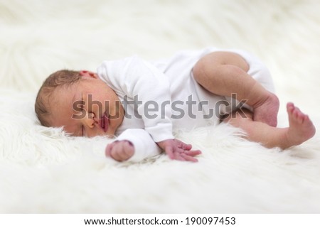 Newborn baby is lying on a sheepskin. Little girl is dreaming sweet things. Baby is 5 days old.