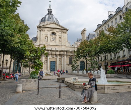 PARIS, FRANCE - AUGUST 18, 2015: An older woman and others are reading books while sitting beside the water fountains of Place de la Sorbonne in front of Eglise de la Sorbonne on a summer afternoon.