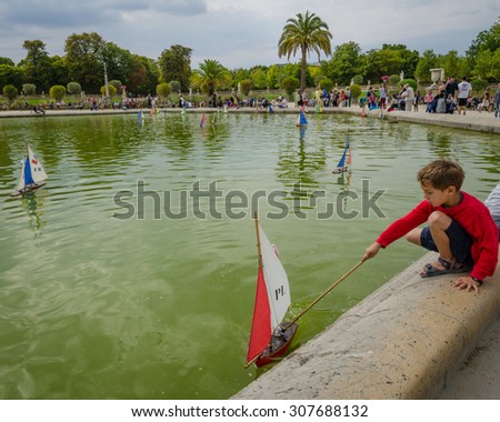 PARIS, FRANCE - AUGUST 18, 2015: A boy is playing with a sailboat in the pond at the Luxembourg Gardens on a summer afternoon.