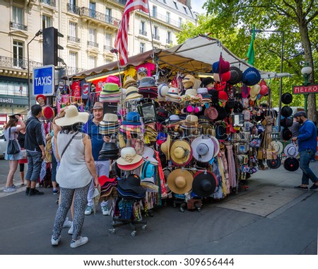 PARIS, FRANCE - AUGUST 10, 2015: People try on fashionable hats sold at a corner souvenir stand in the Opera district on a hot, summer day.