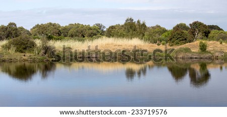 Panoramic reflections in the early morning light of the  calm peaceful blue  lake  at Big Swamp, Bunbury,Western Australia, after the sun   has risen  over the eastern horizon on a cloudy spring day.
