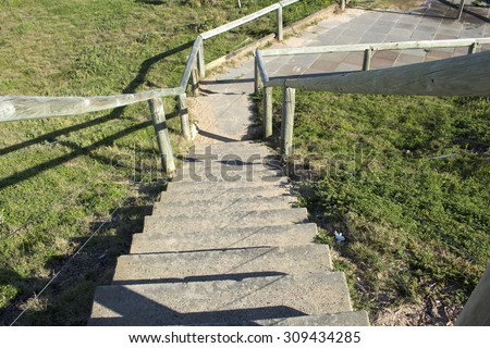 Wooden  pole and concrete  steps  with green vegetation on either side  leading down to the ocean at Ocean Beach Bunbury Western Australia on a calm   sunny  winter morning.