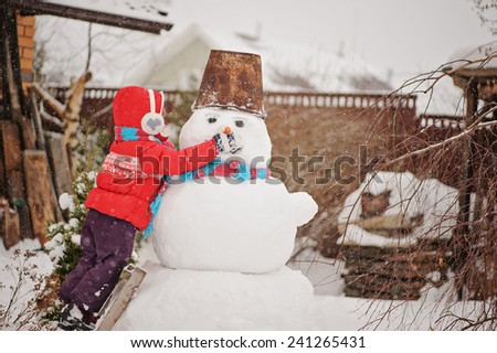 child girl in red coat on ladder making snowman in winter garden