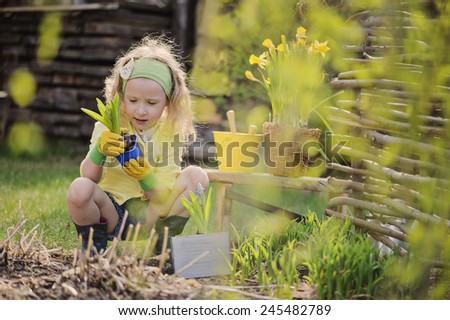 Adorable child girl in yellow cardigan and rubber gloves plays little gardener and planting flowers in spring garden
