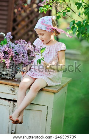 cute child girl in pink plaid dress cuts lilacs from bouquet in spring garden