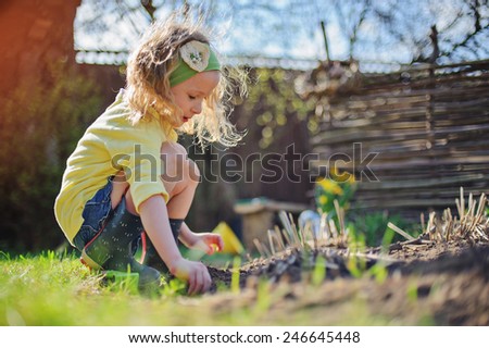 adorable child girl in sunny spring garden planting flowers