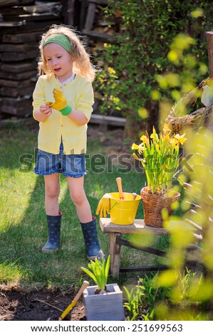child girl plays little gardener and wearing rubber gloves in spring