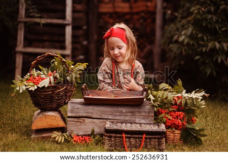 smiling child girl in red headband making rowan berry beads in autumn garden